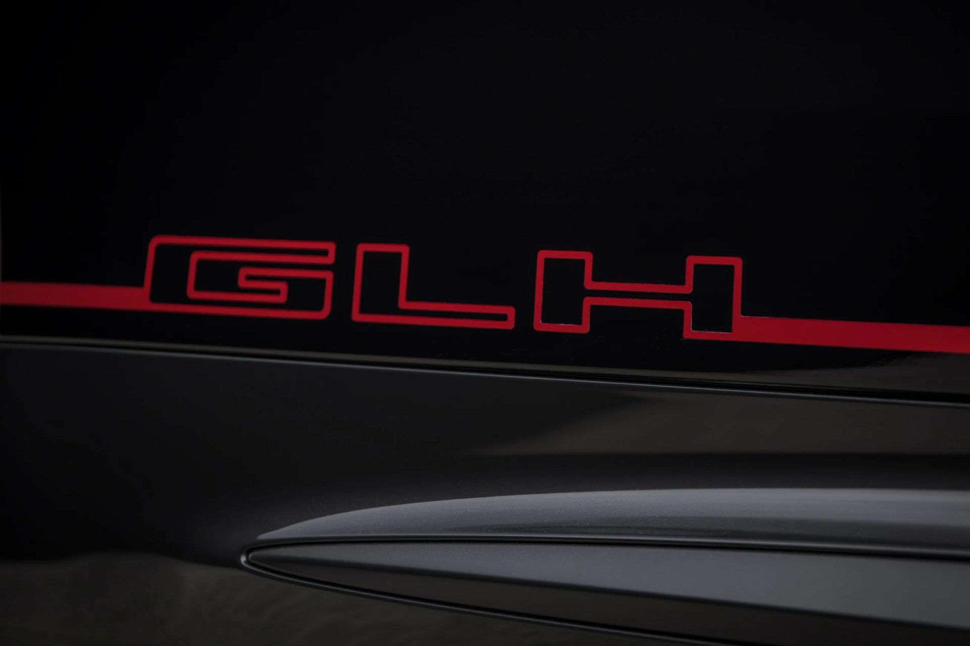 Red "GLH" emblem on a glossy black surface above a matte black vent or panel.
