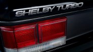 Close-up of a black car's rear with "Shelby Turbo" decal above red and white taillights.