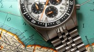 Close-up of a stainless steel chronograph watch with a white dial and black subdials on a vintage map background.