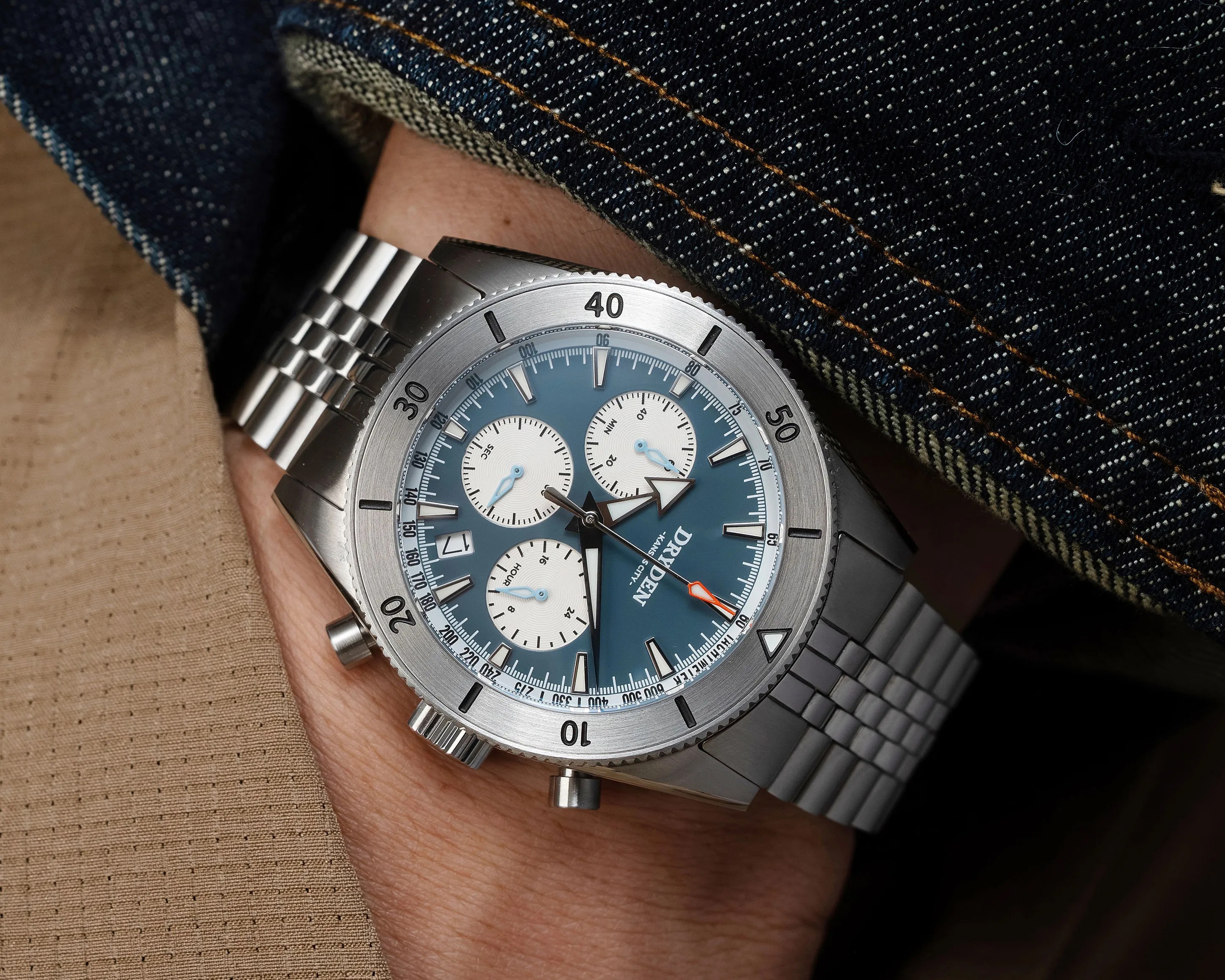Stainless steel chronograph wristwatch with blue dial and white subdials worn under a denim jacket cuff.