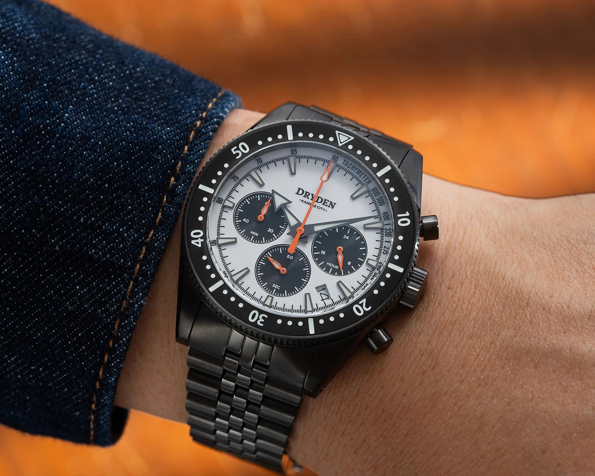 Black metal wristwatch with white dial and three black subdials worn on a wrist.