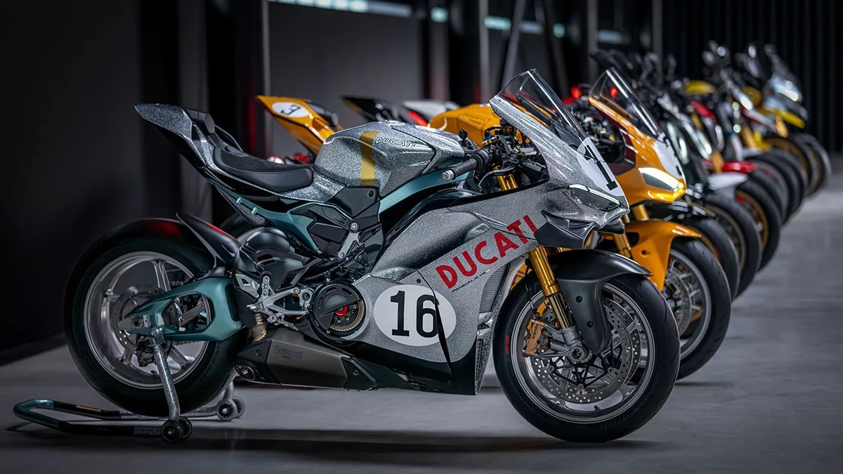 Silver Ducati racing motorcycle with red logo and number 16, parked in a row with other motorcycles.