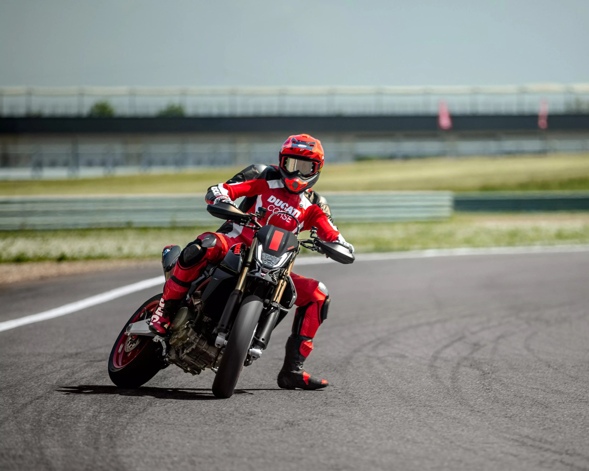 Motorcyclist in red Ducati racing gear leaning into a turn on a black Ducati motorcycle on a racetrack.