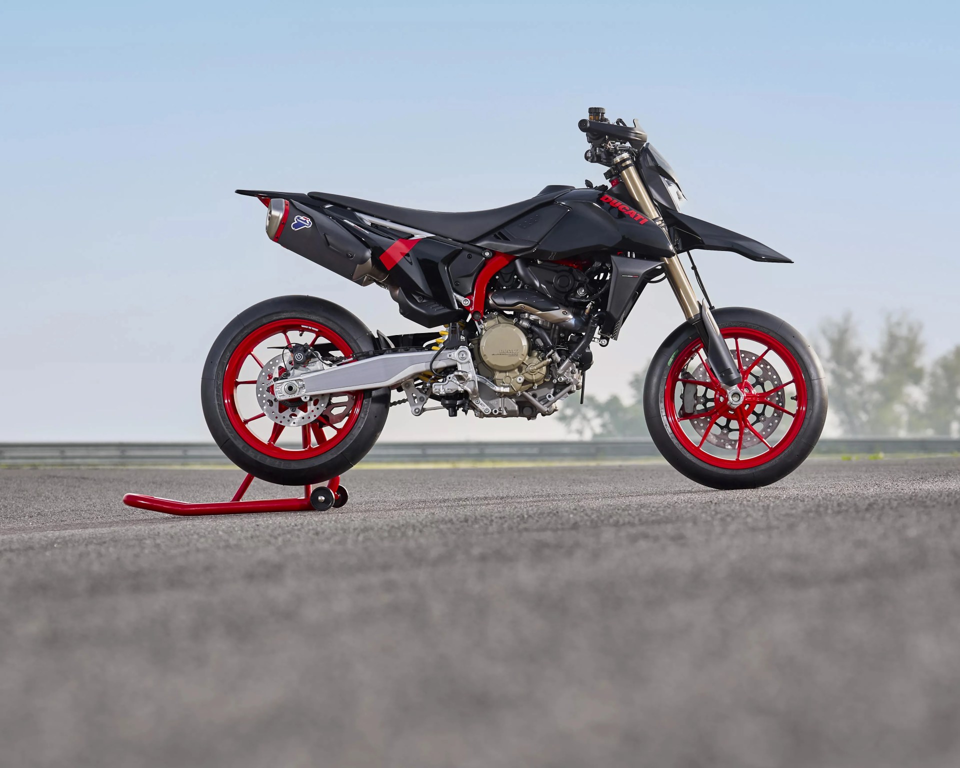 Black Ducati motorcycle with red frame and wheels on a red rear stand on asphalt.