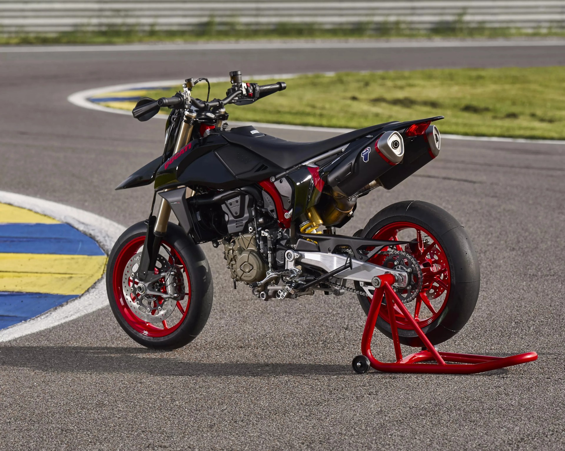 Black Ducati motorcycle with red wheels and dual exhausts on a racetrack stand.