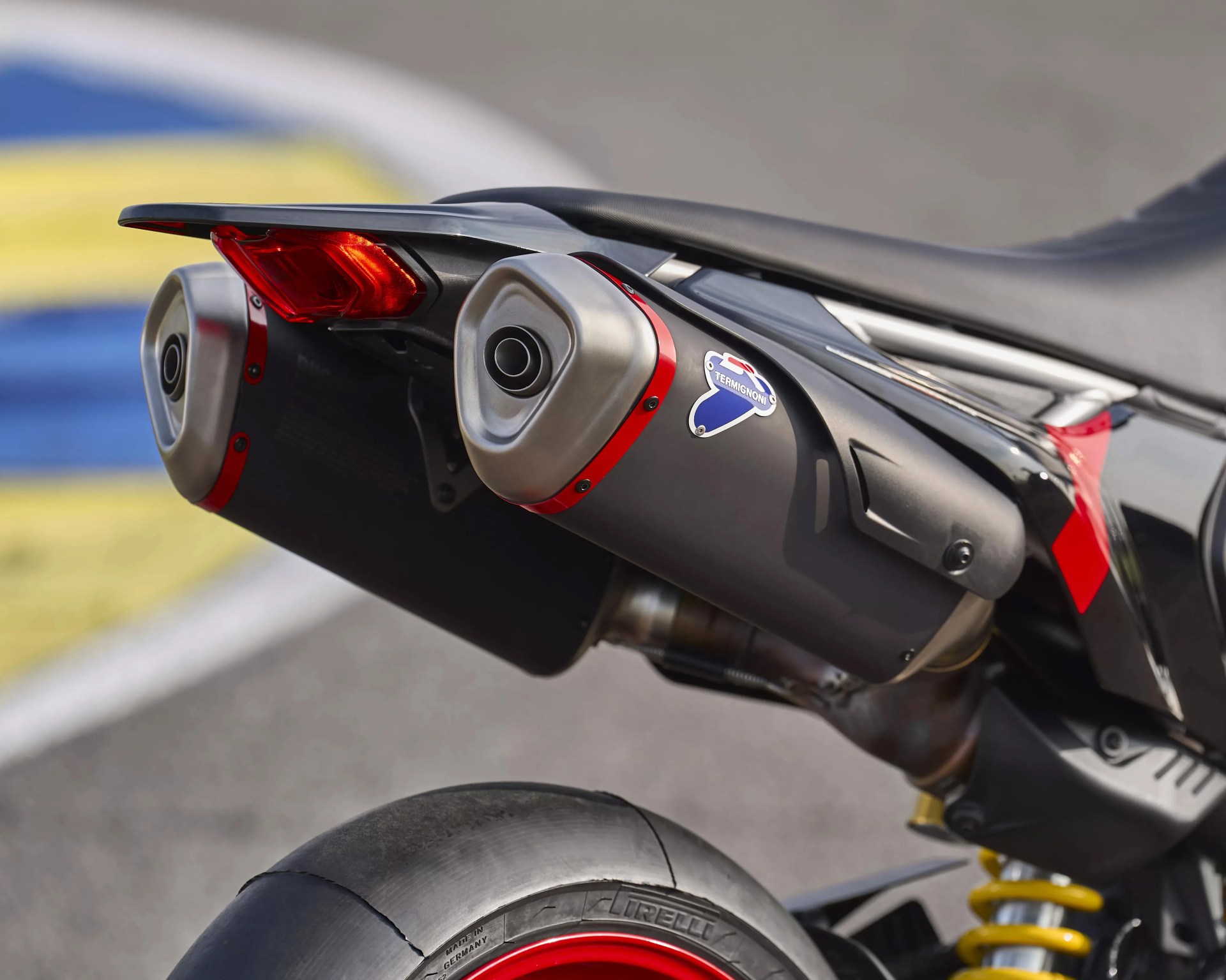Close-up of a motorcycle's rear section showing dual Termignoni exhausts, red taillight, and Pirelli tire with red rim.