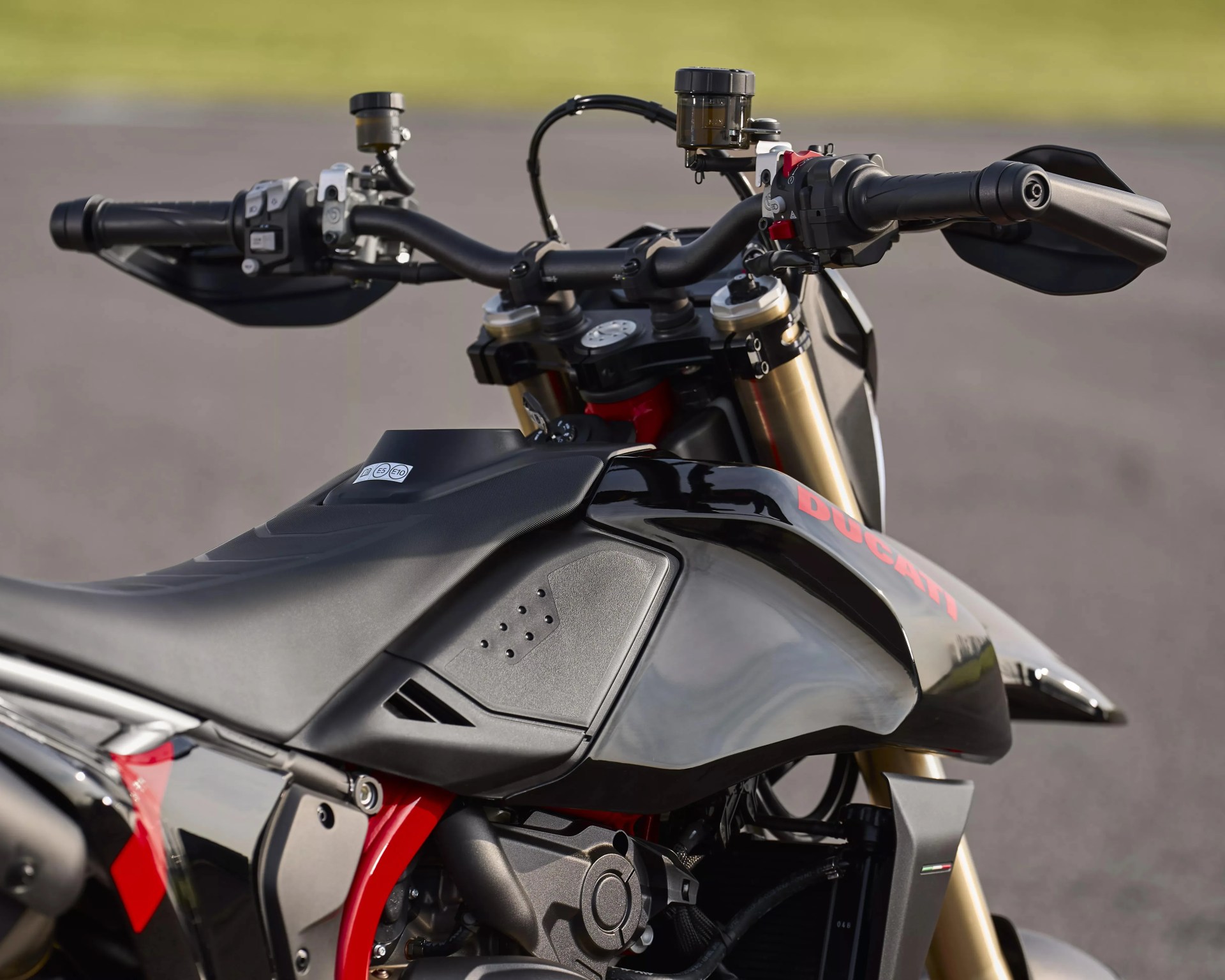 Close-up of black Ducati motorcycle fuel tank, seat, and handlebars with gold front forks.