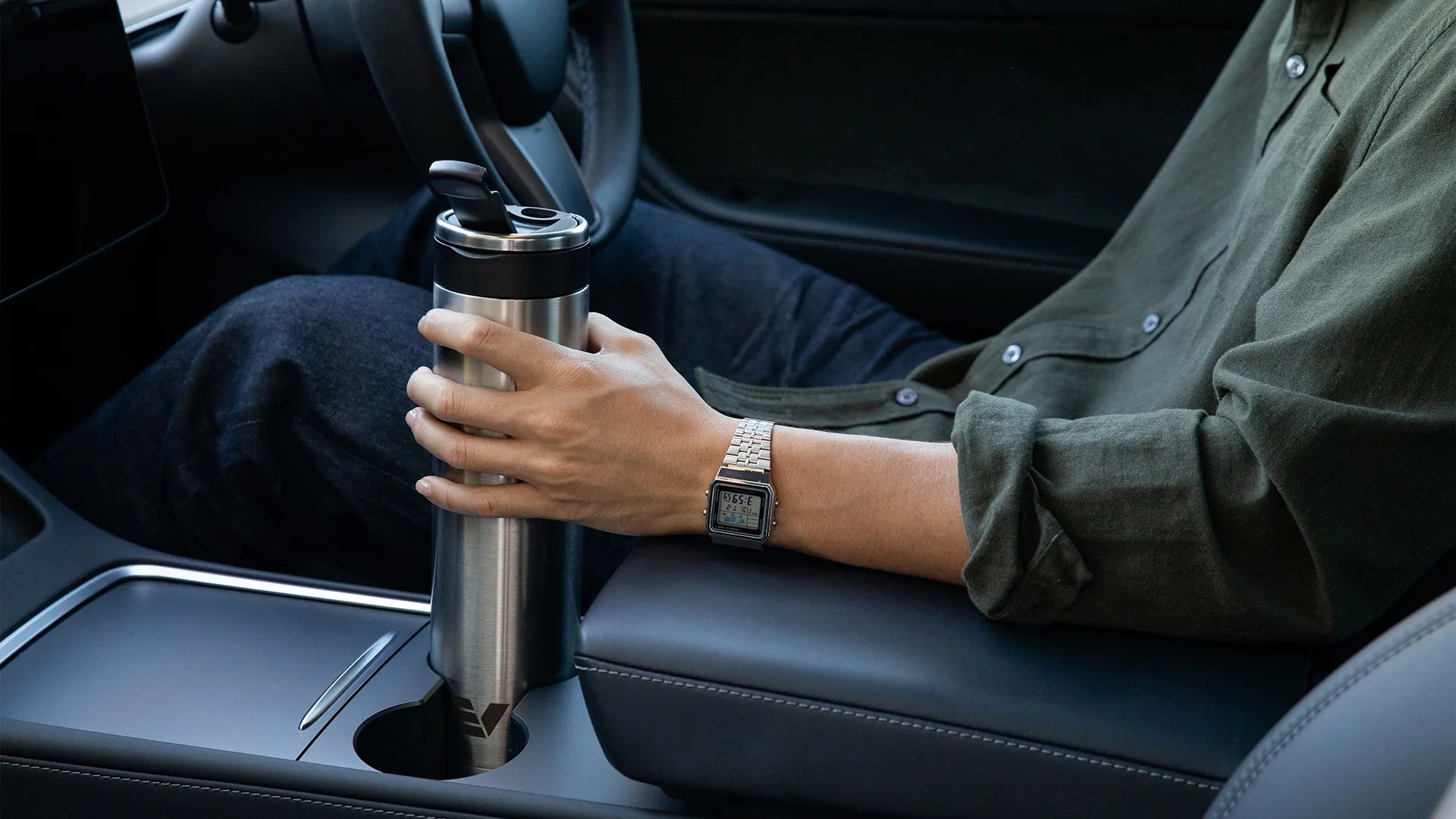 Hand holding a stainless steel travel mug with black lid inside a car cup holder.