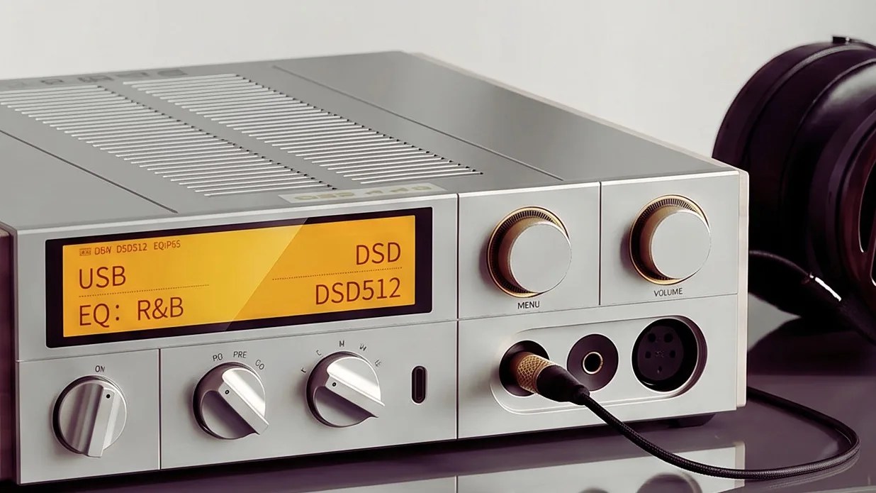 Silver digital audio player with yellow display showing USB and DSD512, connected to black headphones.