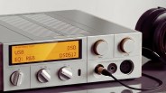 Silver digital audio player with yellow display showing USB and DSD512, connected to black headphones.