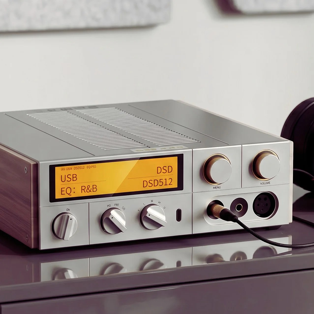 Silver audio amplifier with wooden side panels, yellow digital display, and multiple control knobs on a reflective surface.