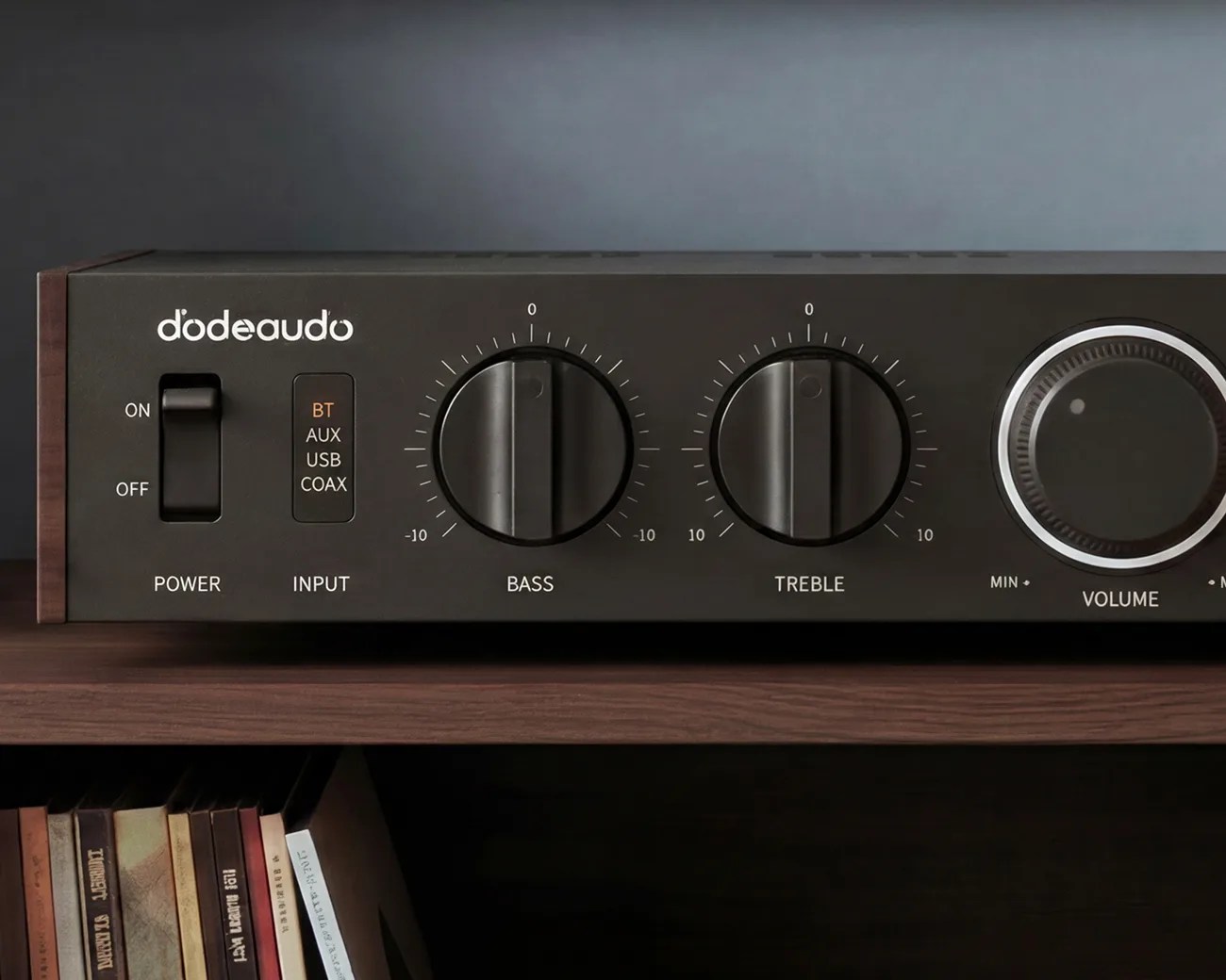 Black dodeaudo audio amplifier with bass, treble, and volume knobs on a wooden shelf.