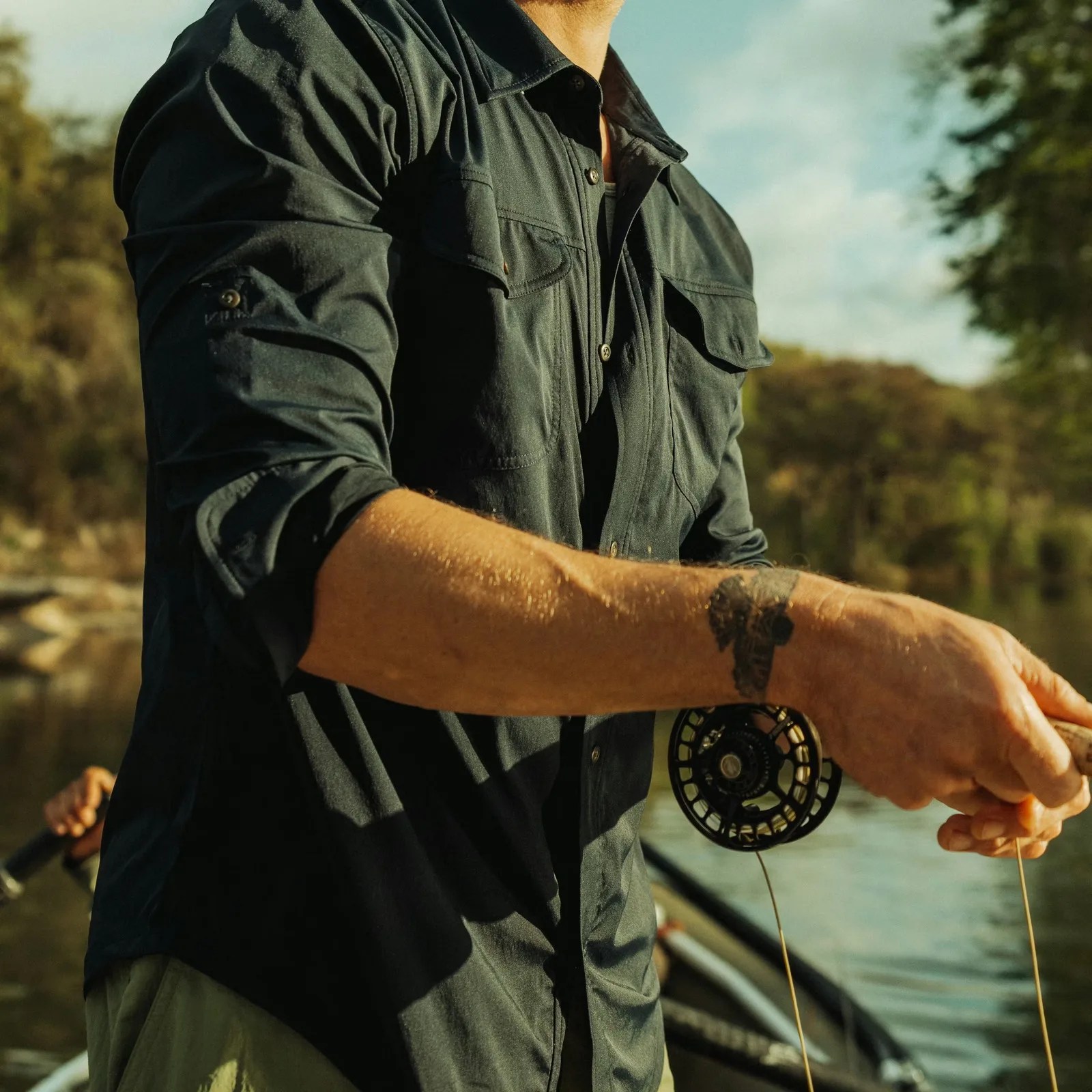 Dark green long-sleeve button-up shirt with chest pockets worn by a person holding a fishing reel.