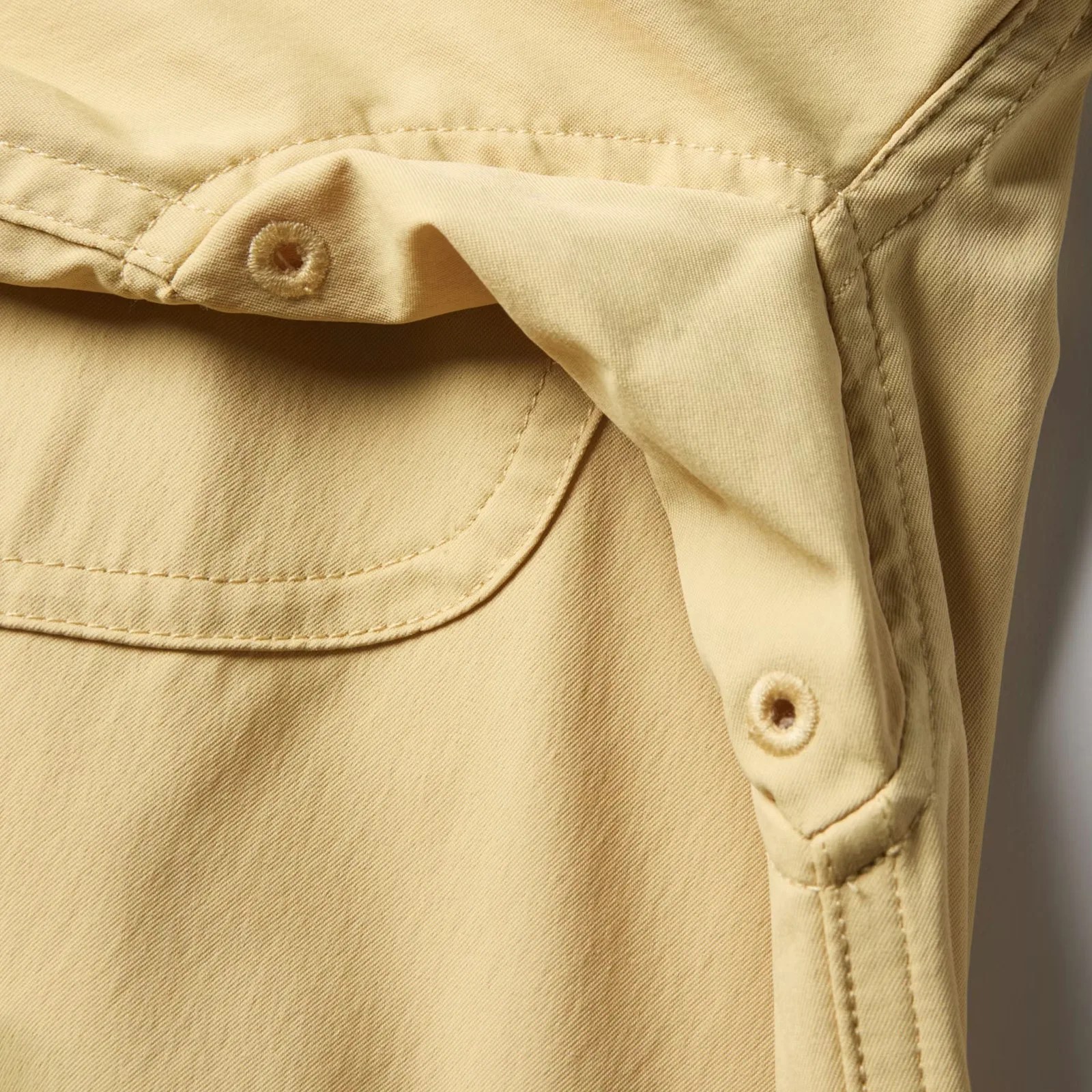 Close-up of beige fabric with stitched seams and buttonholes, likely part of a garment or bag.