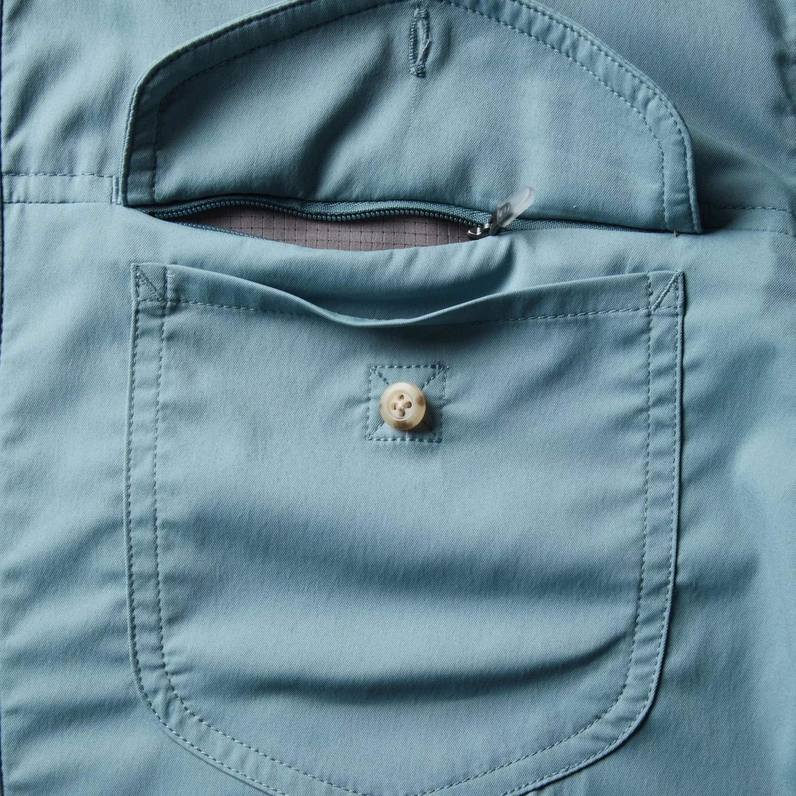 Light blue fabric pocket with a button and a partially open zipper revealing a gray inner lining.