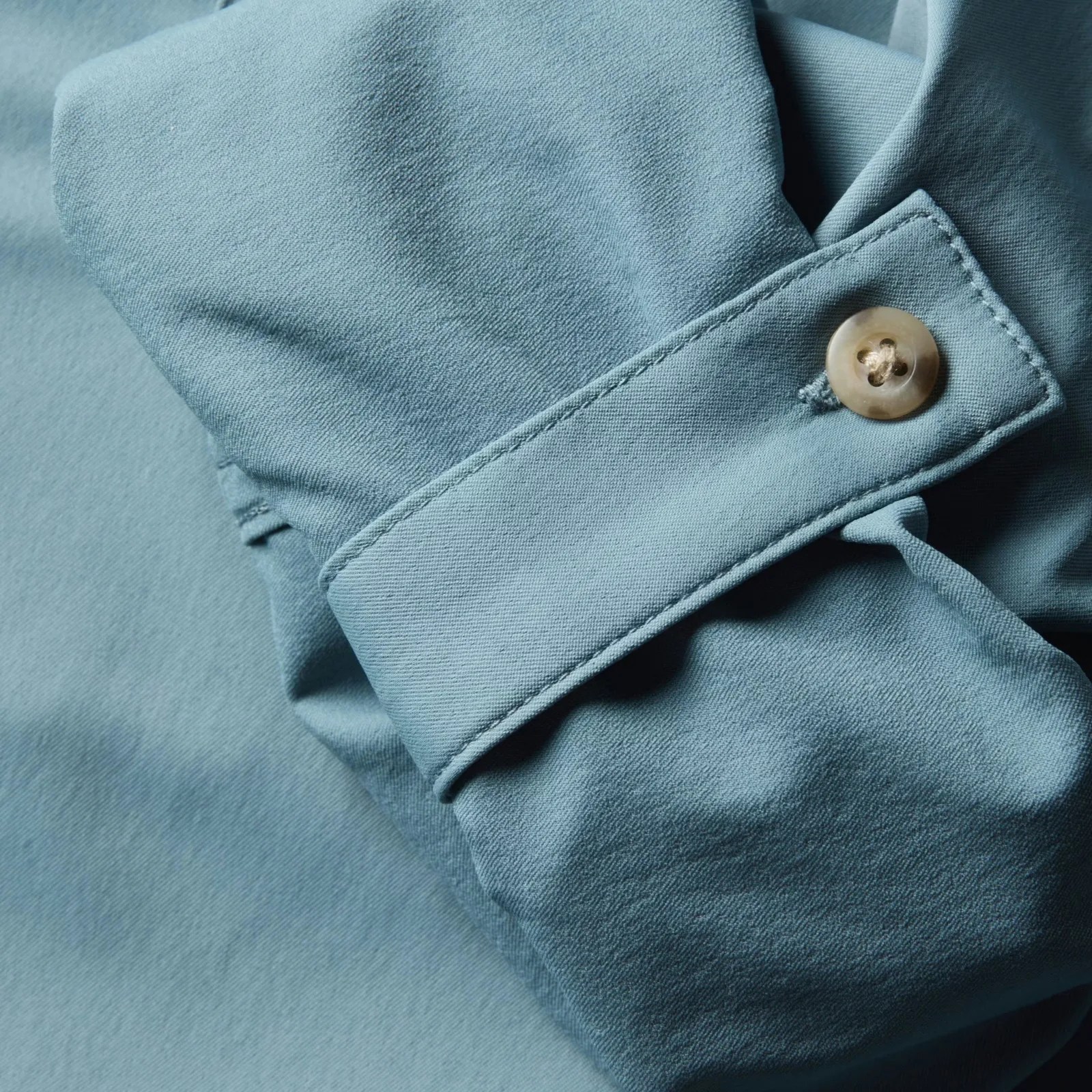 Close-up of a light blue fabric cuff with a beige button and detailed stitching.