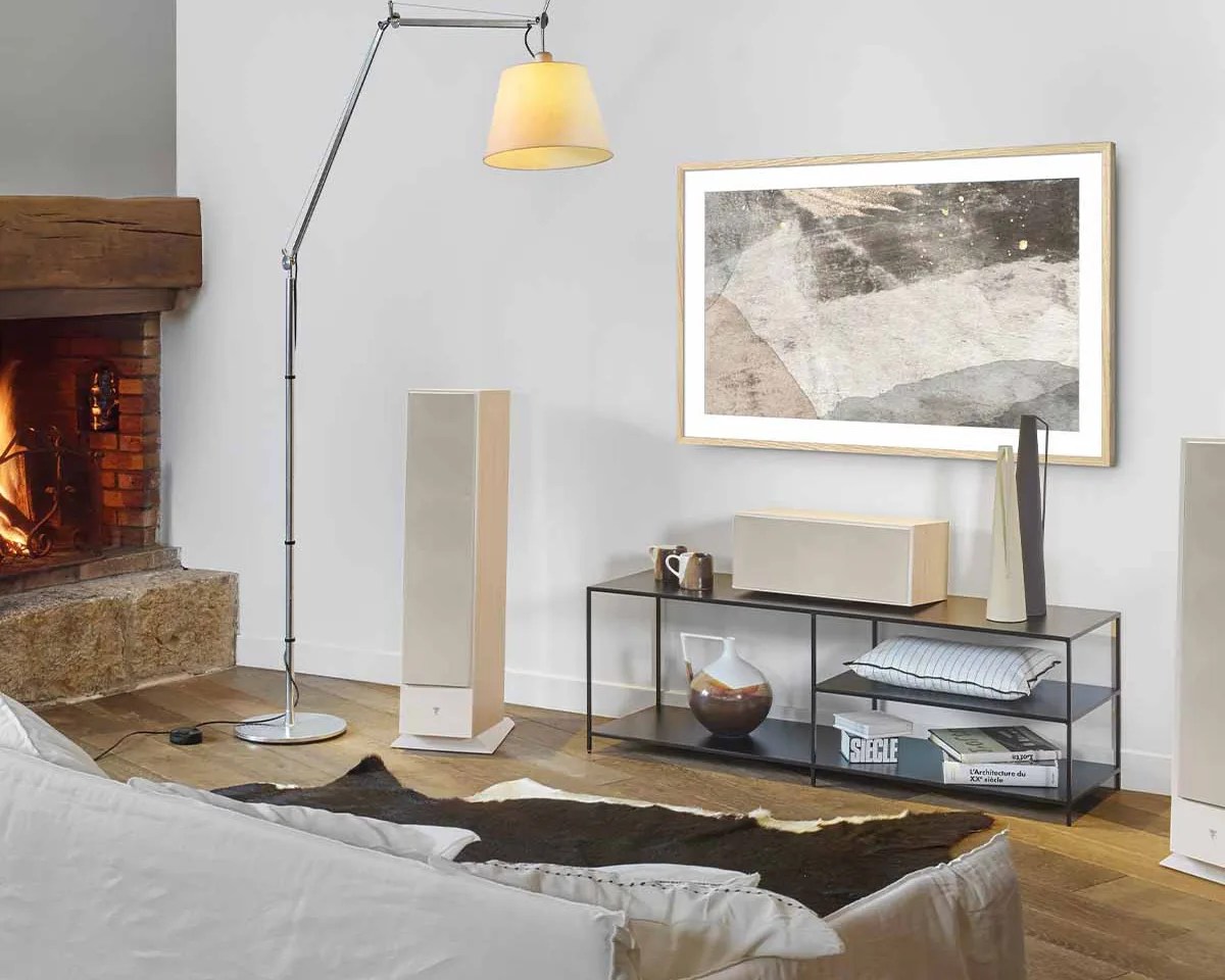 Modern living room corner with beige floor-standing speakers, black metal TV stand with decor, and a lit fireplace.