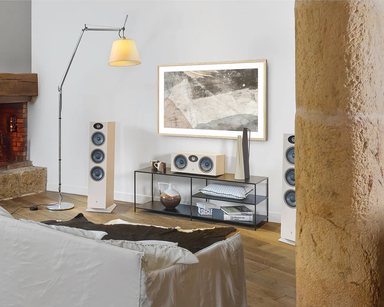 Living room with white floor-standing speakers, a black metal TV stand with decor, a modern floor lamp, and abstract wall art.