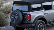 Rear side of a silver SUV with a black soft top, spare tire cover featuring a horse logo, and off-road tires.