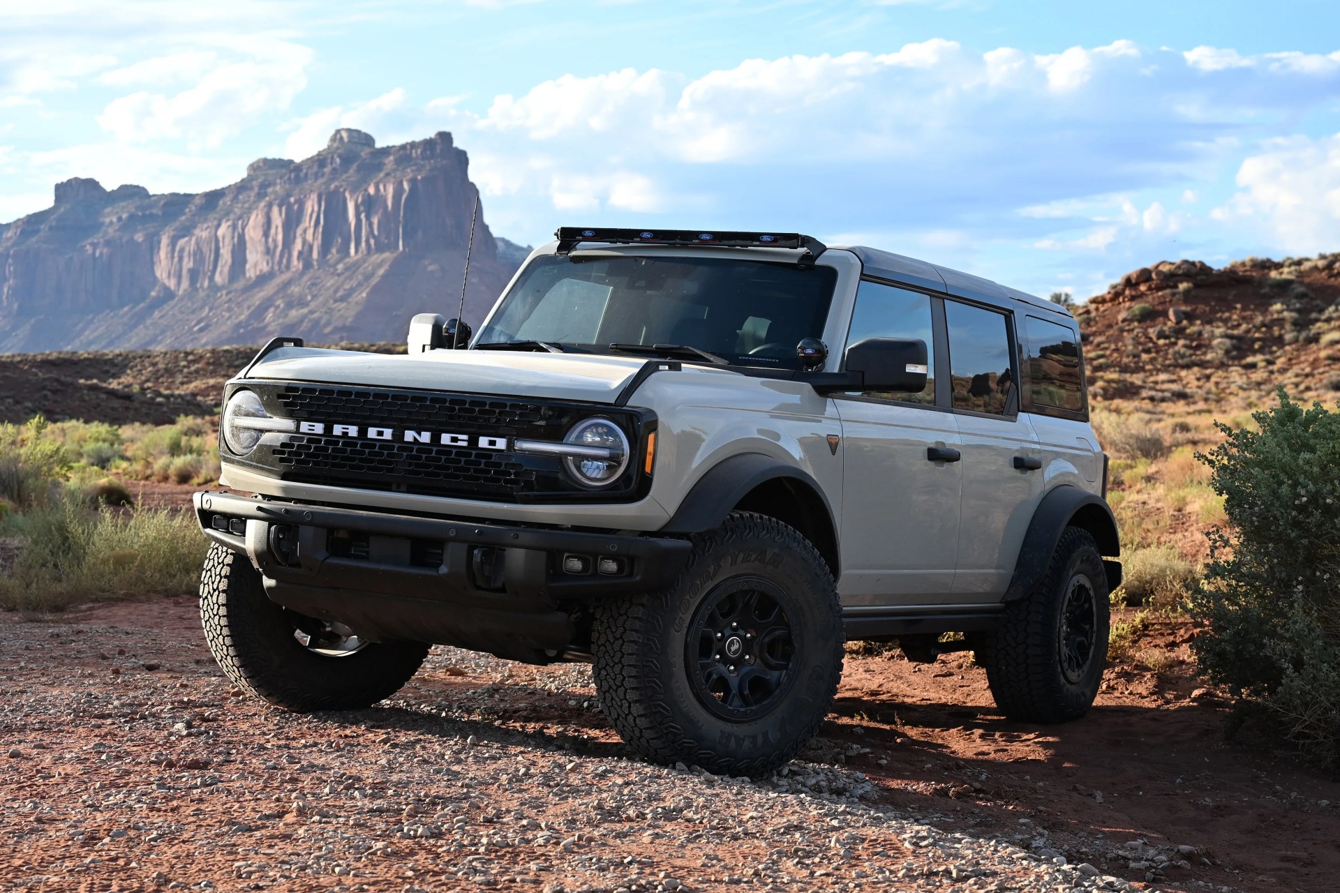 White Ford Bronco SUV with black trim parked on rocky terrain with mountains in the background.