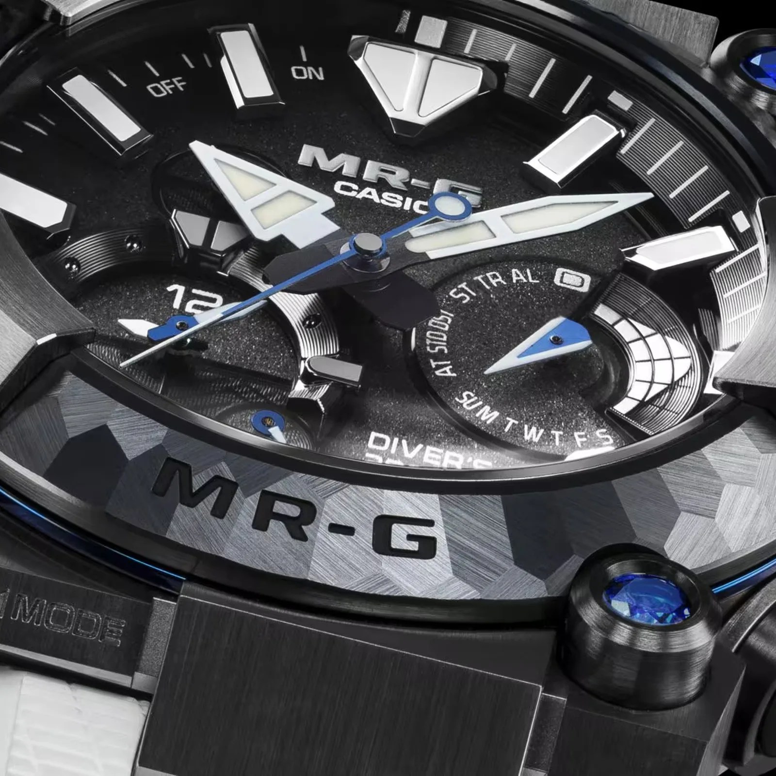 Close-up of a Casio MR-G watch face with black dial, white and blue hands, and textured metal bezel.