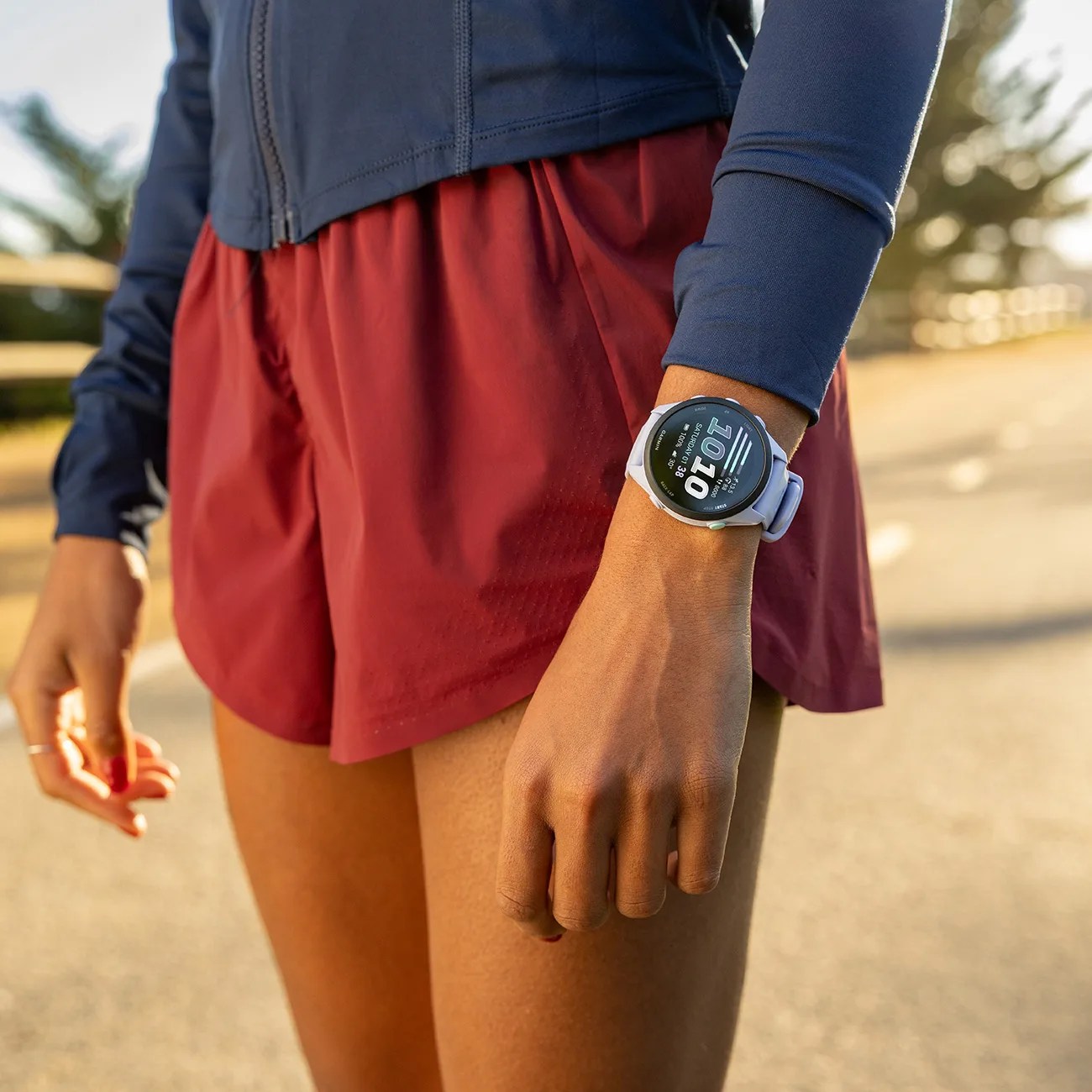 Close-up of a person wearing a white smartwatch with a digital display on their wrist, dressed in a navy jacket and red shorts.
