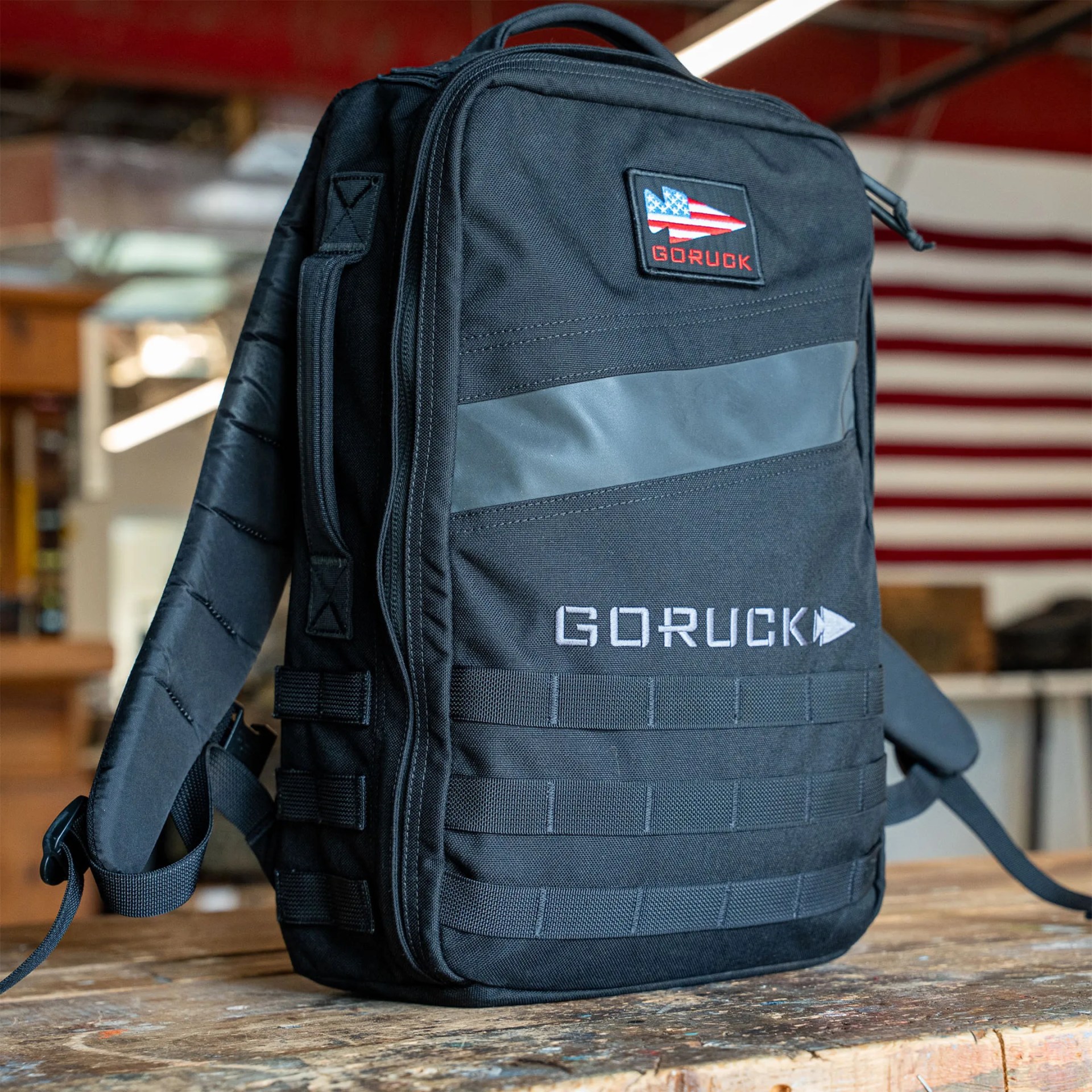 Black GORUCK backpack with American flag patch on a wooden surface in an indoor setting.
