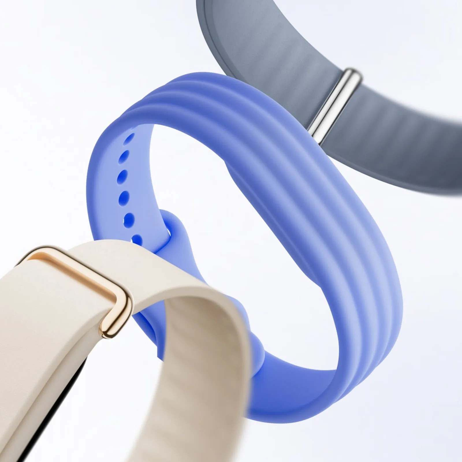 Three close-up silicone watch bands in cream, blue, and gray colors with textured ridges and holes for adjustment.