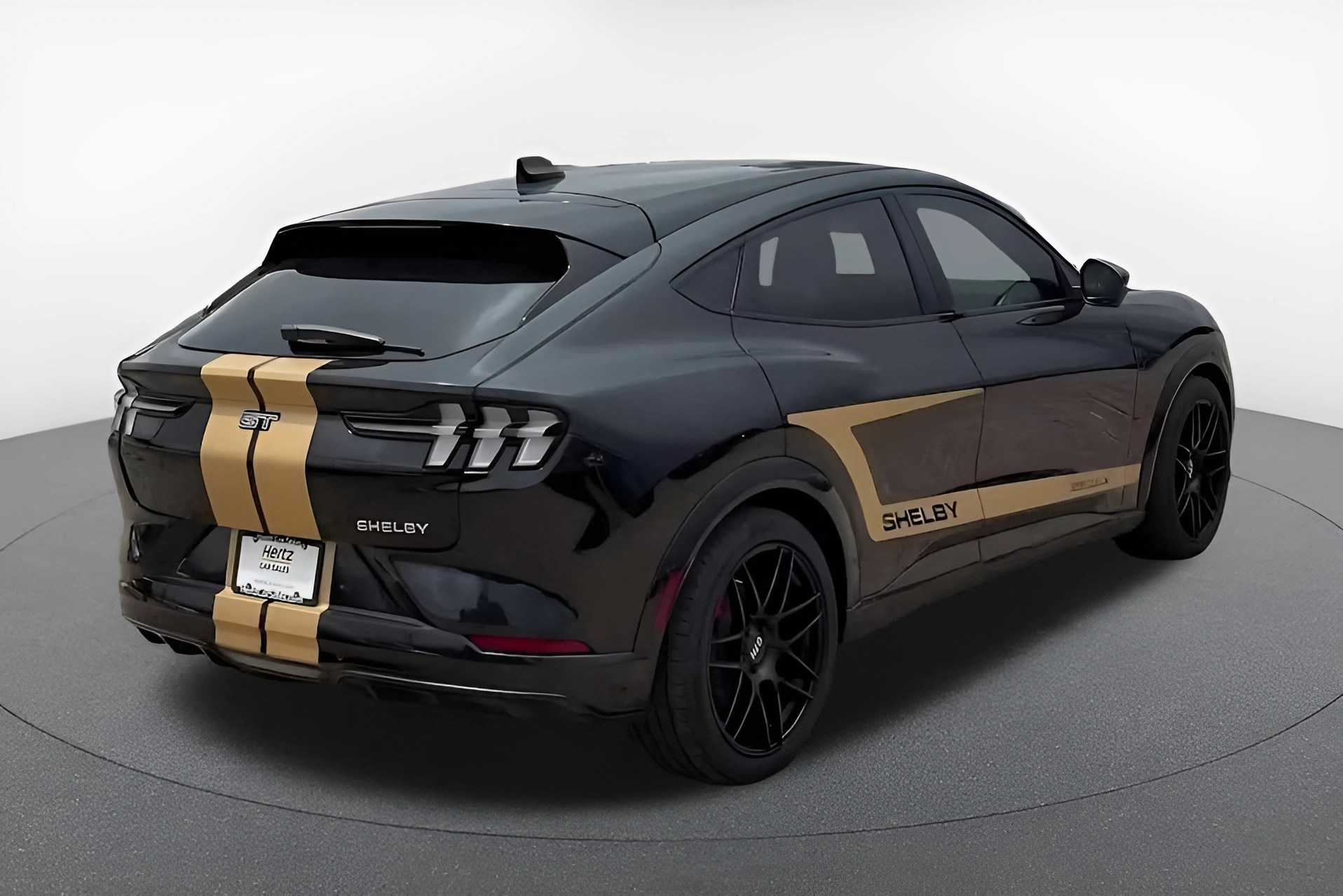 Black Shelby Mustang Mach-E GT with gold racing stripes and black wheels in a studio.