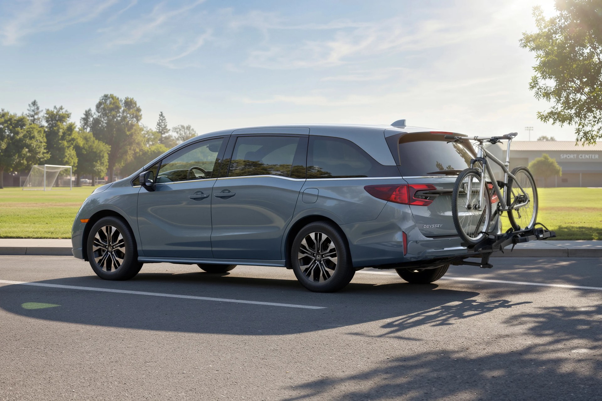 Blue Honda Odyssey minivan with tinted windows parked on a street with a bicycle mounted on a rear bike rack.