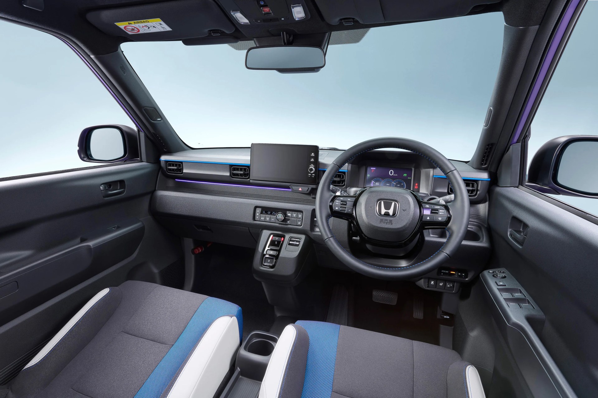 Interior of a Honda car showing a black steering wheel with blue stitching, digital dashboard, touchscreen display, and gray and blue fabric seats.