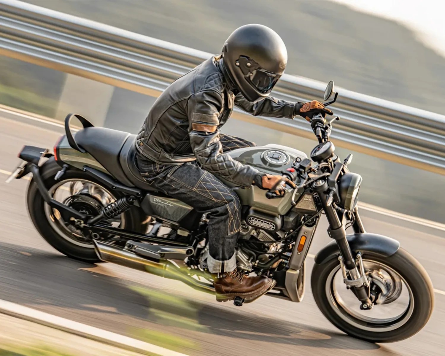 Person wearing a black helmet, leather jacket, and brown boots riding a green and black motorcycle on a road.