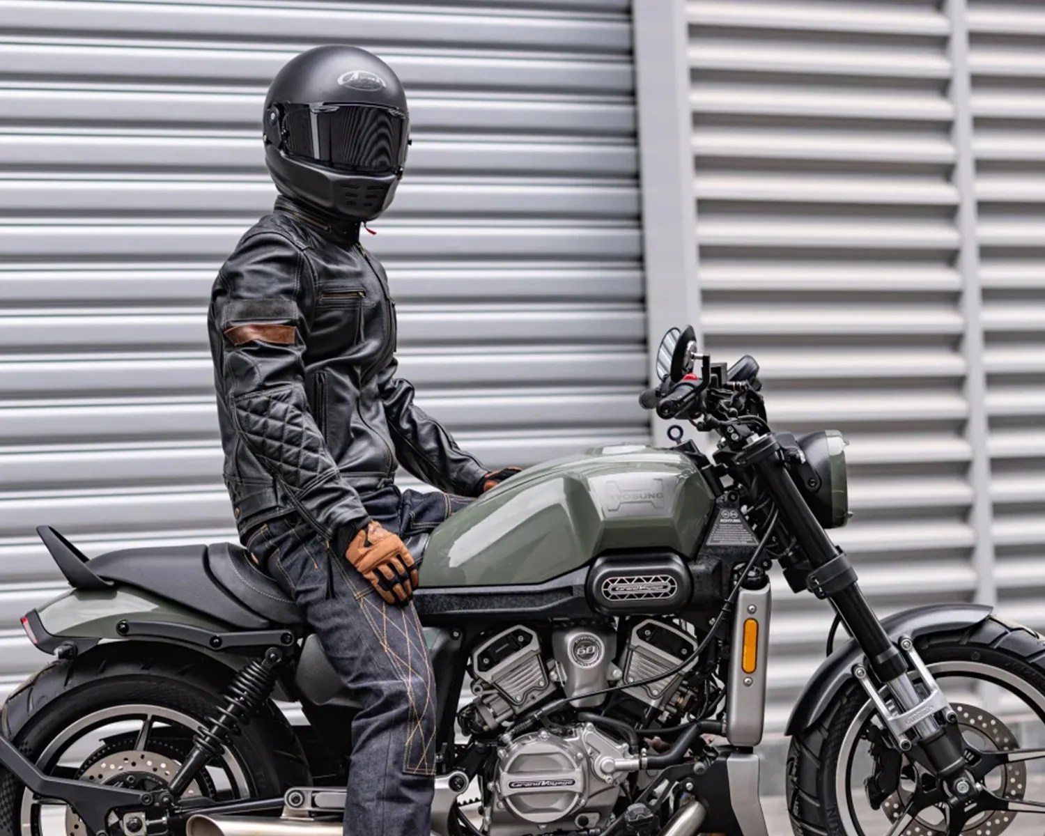 Person wearing a black helmet, black leather jacket, and gloves sitting on a green and black motorcycle.