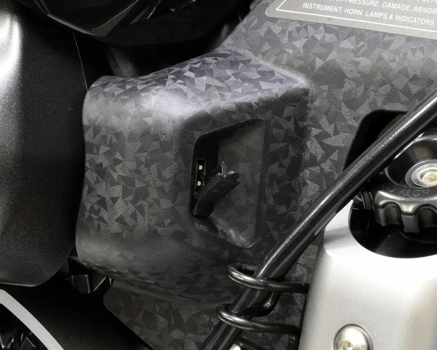 Close-up of a black textured plastic panel with a USB port and a black cable coiled around a silver metal part.