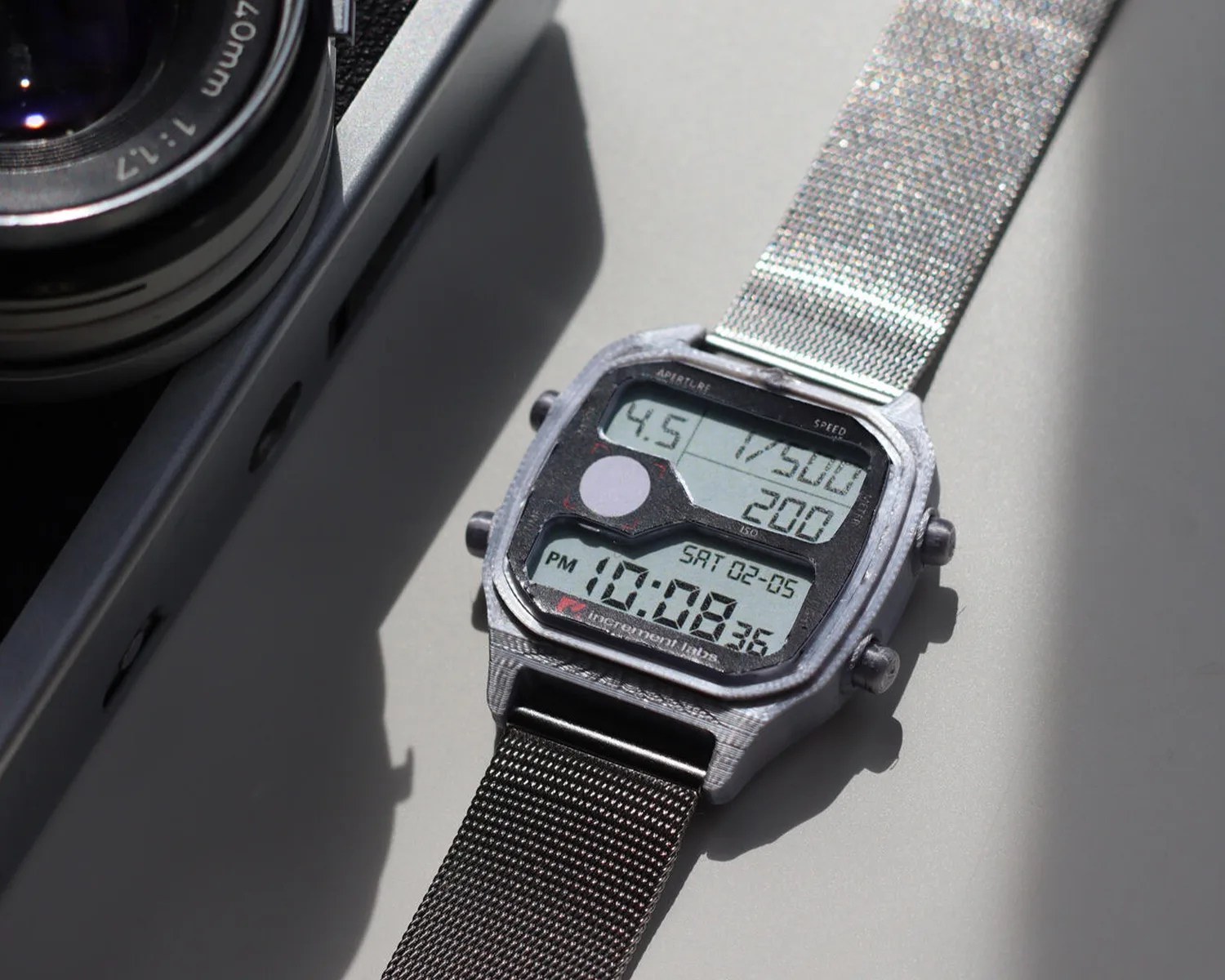 Digital wristwatch with a metal mesh band displaying time, date, and camera settings on the screen.
