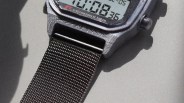 Close-up of a digital watch with a black woven nylon strap and a gray textured case.