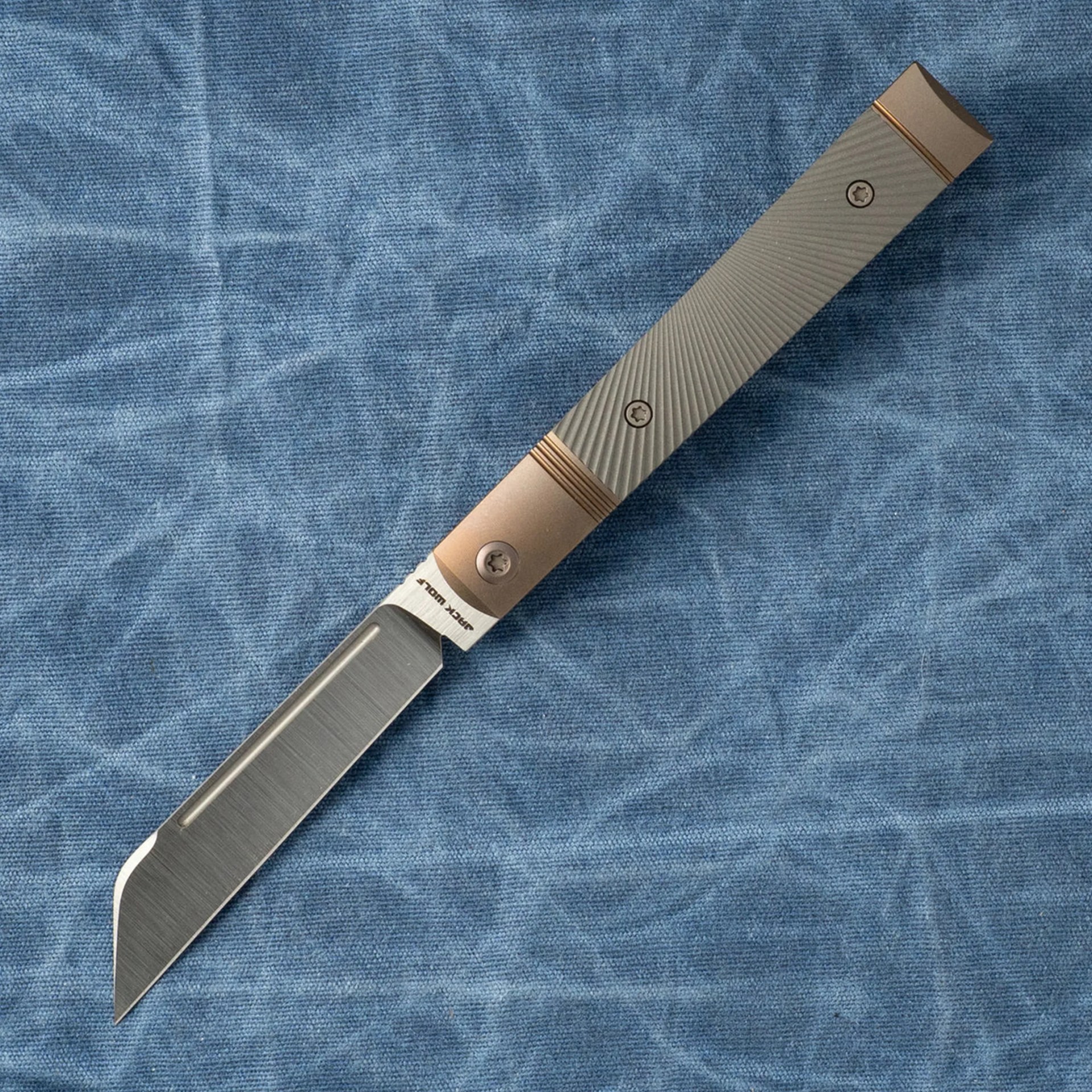 Knife with a textured gray handle and a straight-edged blade on a blue fabric background.