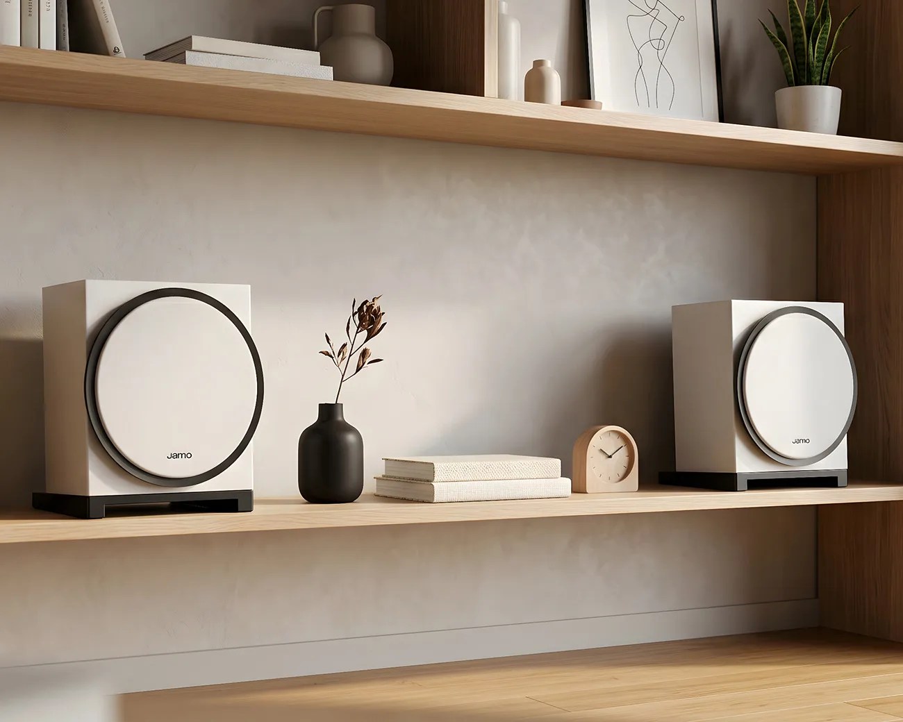 Two white Jamo subwoofers with black bases on a wooden shelf with a black vase, books, and a small wooden clock.
