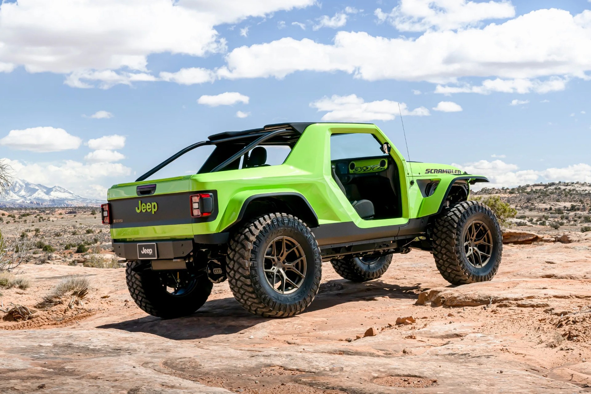 Bright green Jeep Scrambler 392 with large off-road tires on rocky desert terrain under a partly cloudy sky.