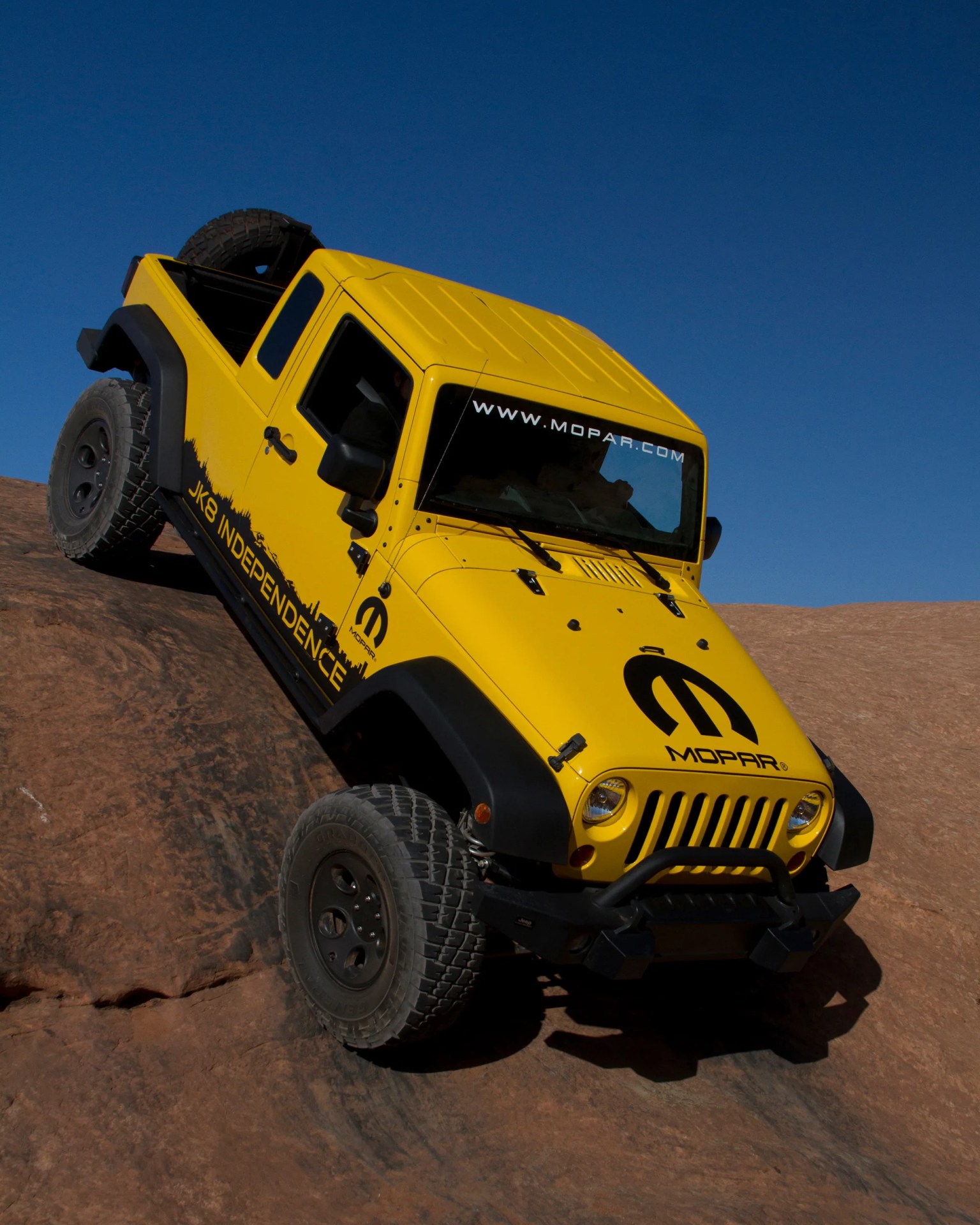 Yellow Jeep Wrangler with Mopar branding climbing rocky terrain under clear blue sky.