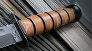 Close-up of a knife handle with stacked leather rings and a black pommel on a metal surface.