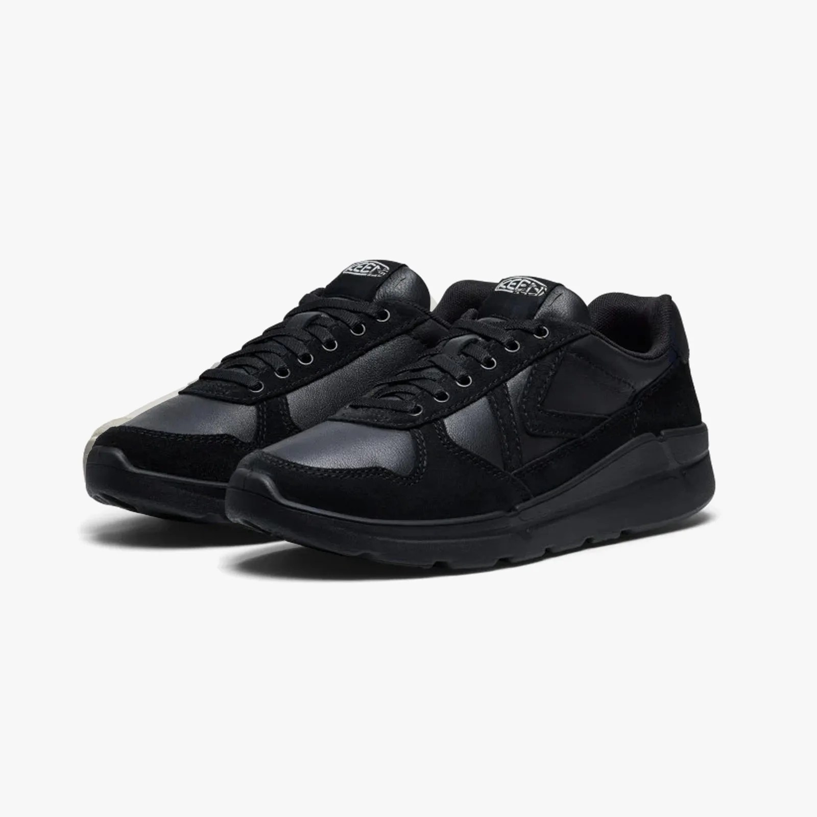 Pair of black low-top sneakers with leather and suede panels and black laces on a white background.
