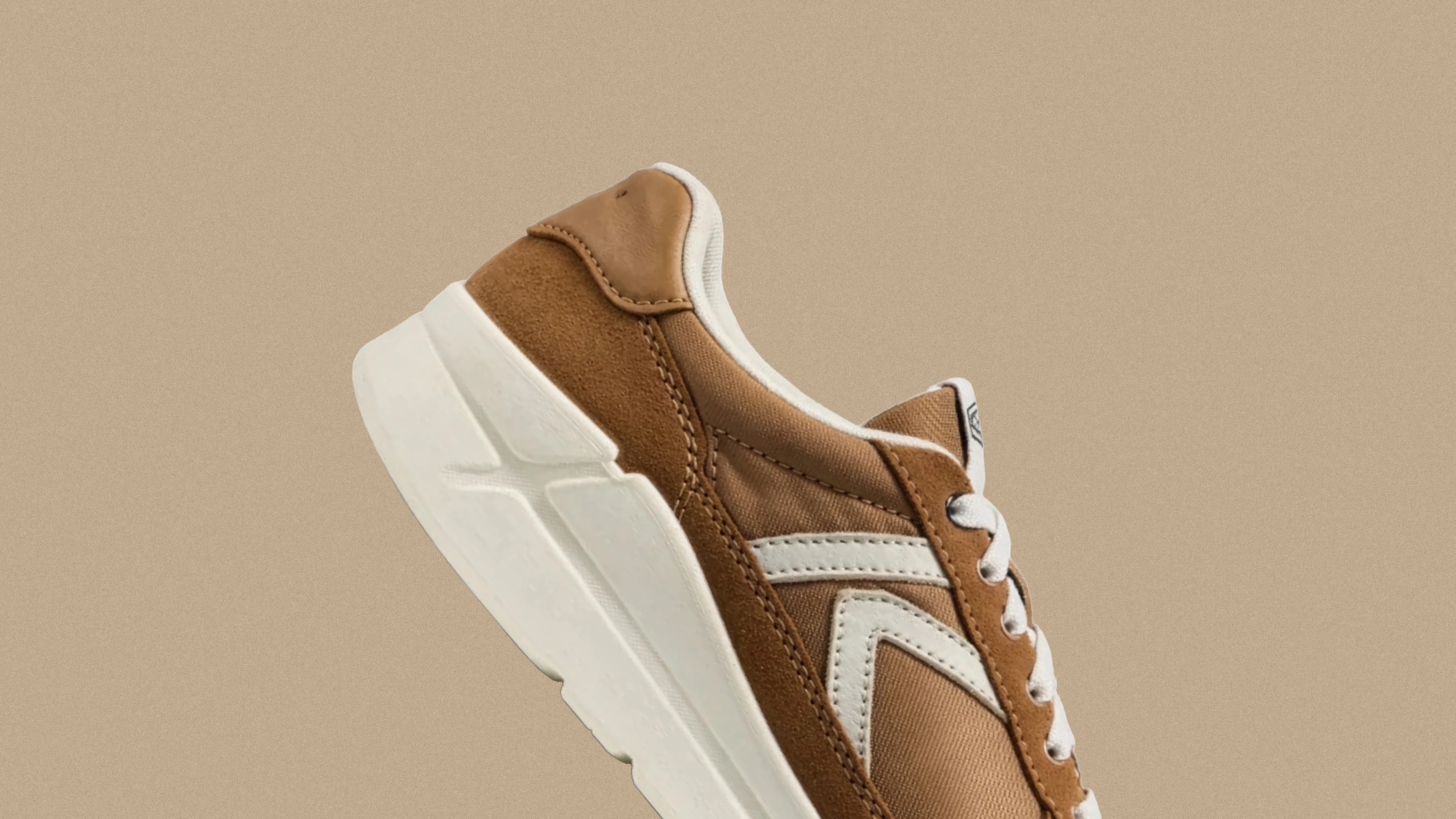 Brown and white sneaker with suede and fabric upper and thick white sole against beige background.