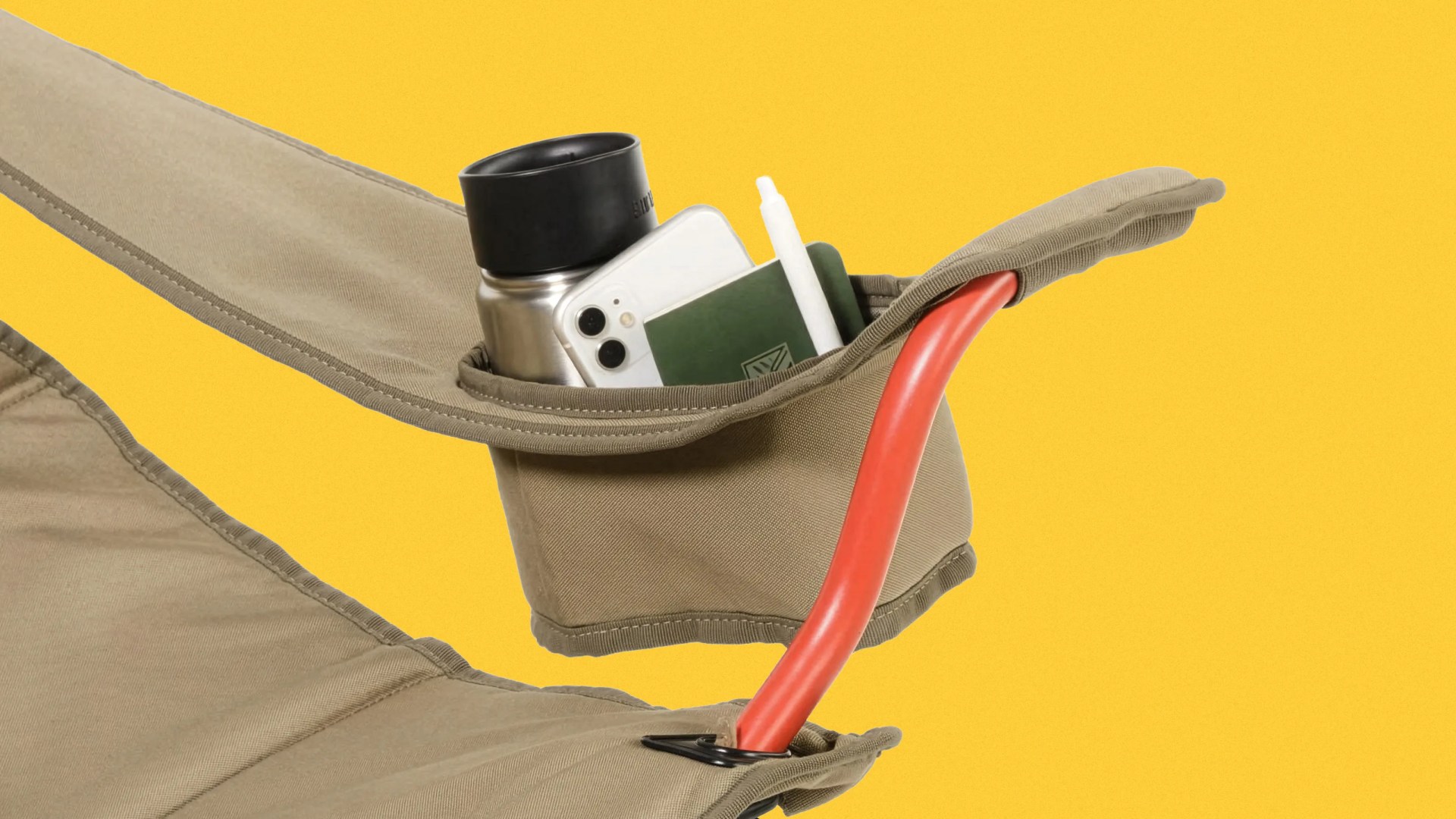 Tan fabric chair armrest pocket holding a silver water bottle, white smartphone, green notebook, and white pen.