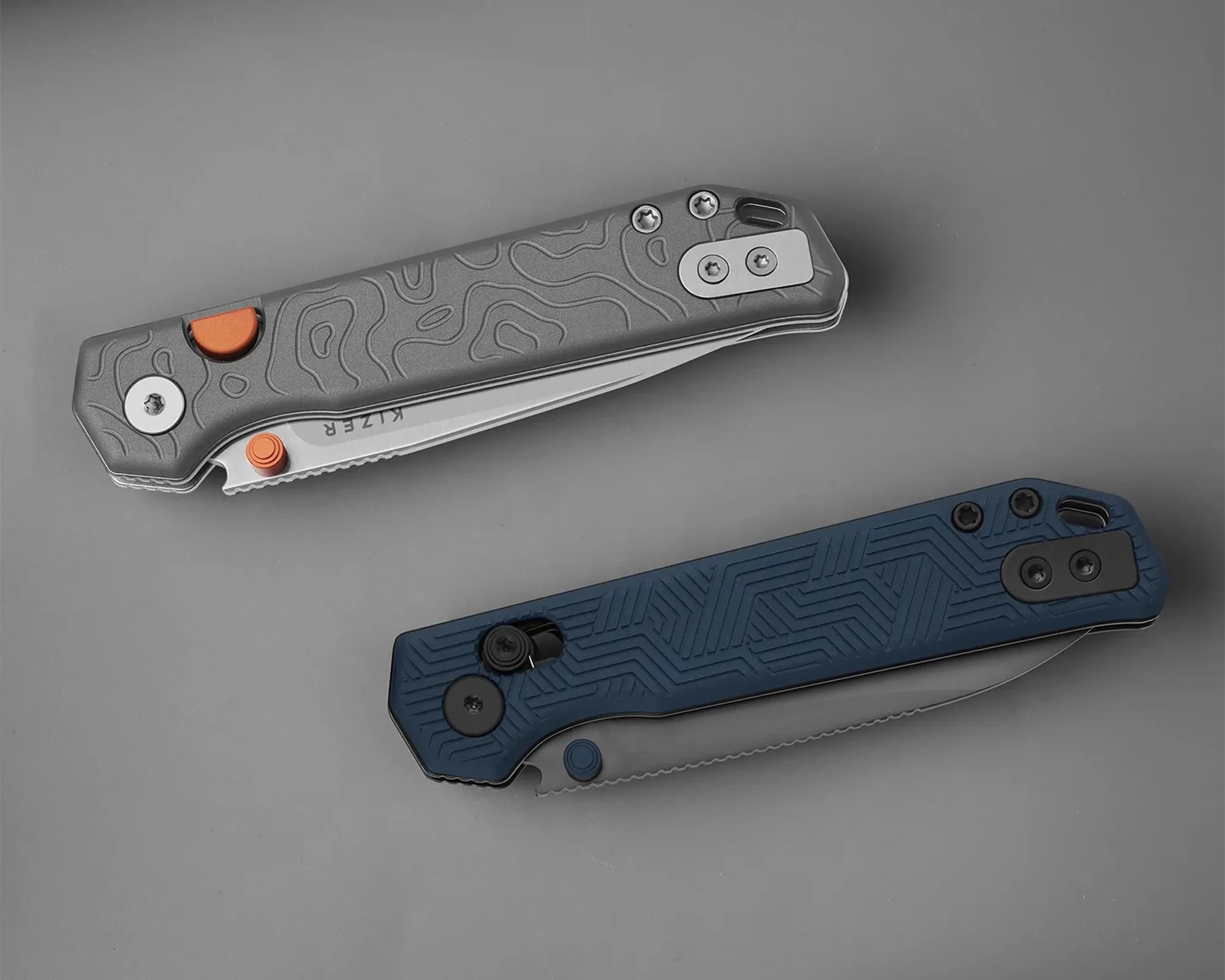 Two folding knives with textured handles, one gray with orange accents and one blue with black accents, on a gray surface.