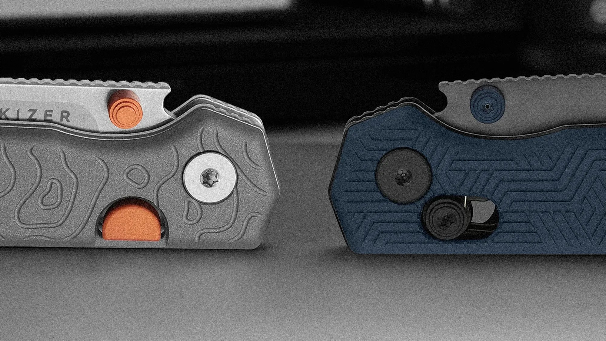 Close-up of two folding knives side by side, one with a gray textured handle and orange accents, the other with a blue textured handle and black screws.