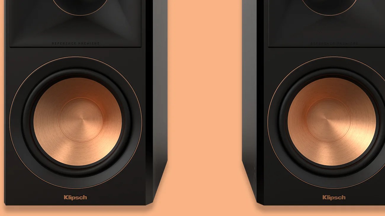 Pair of black Klipsch speakers with copper-colored woofers on a peach background.