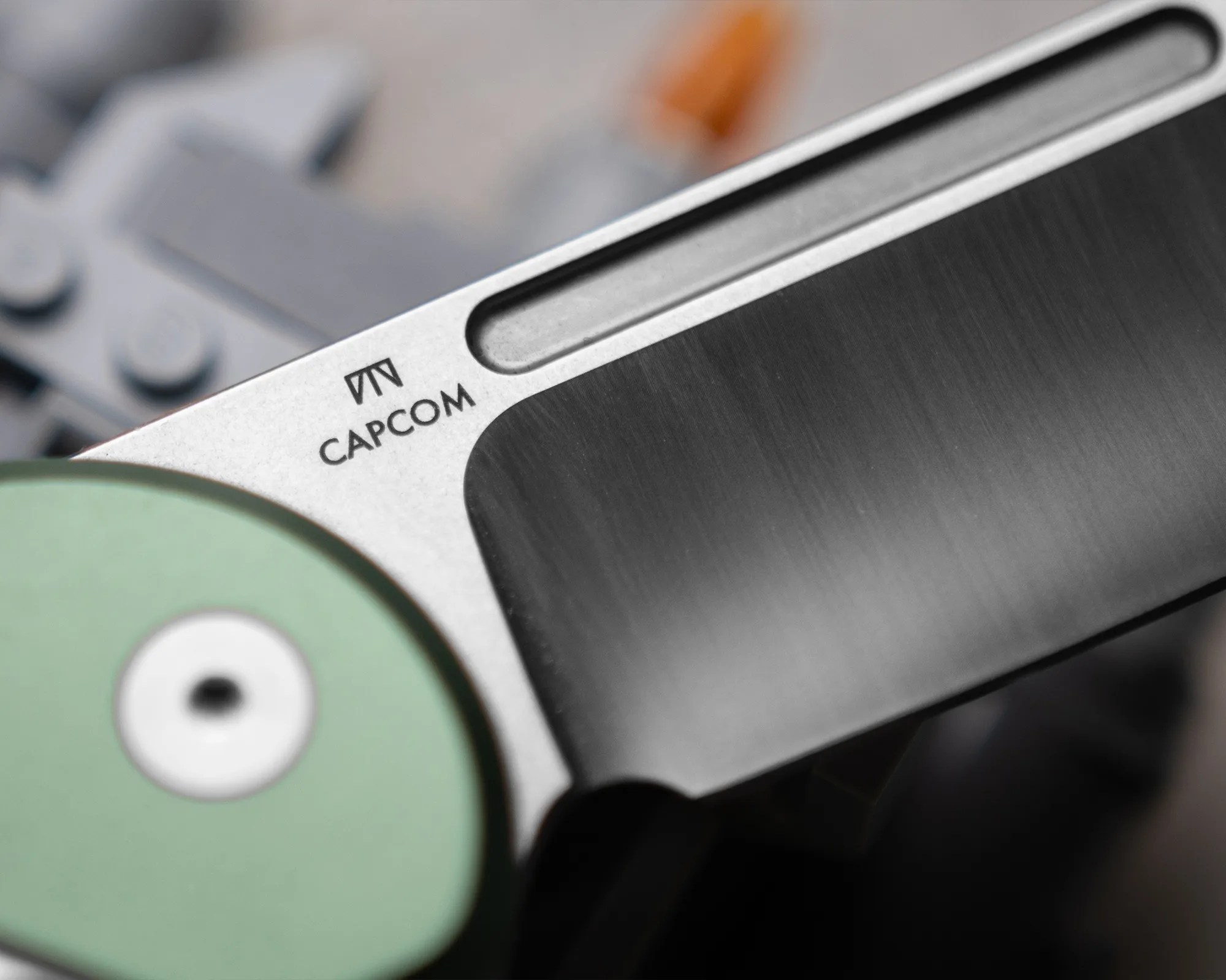 Close-up of a metallic object with a brushed finish and the word "CAPCOM" printed near a green circular part.