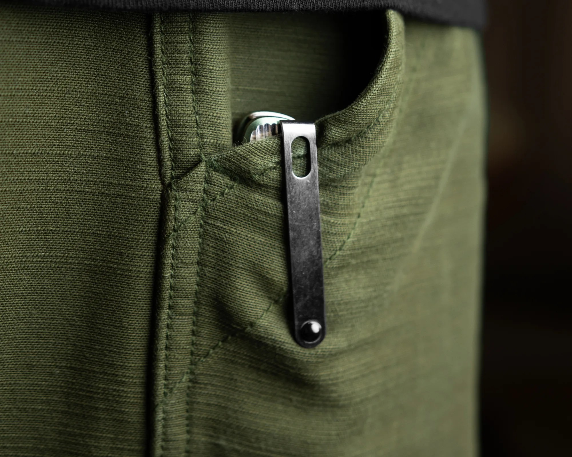 Close-up of a green fabric pocket with a metal clip holding a silver object inside.