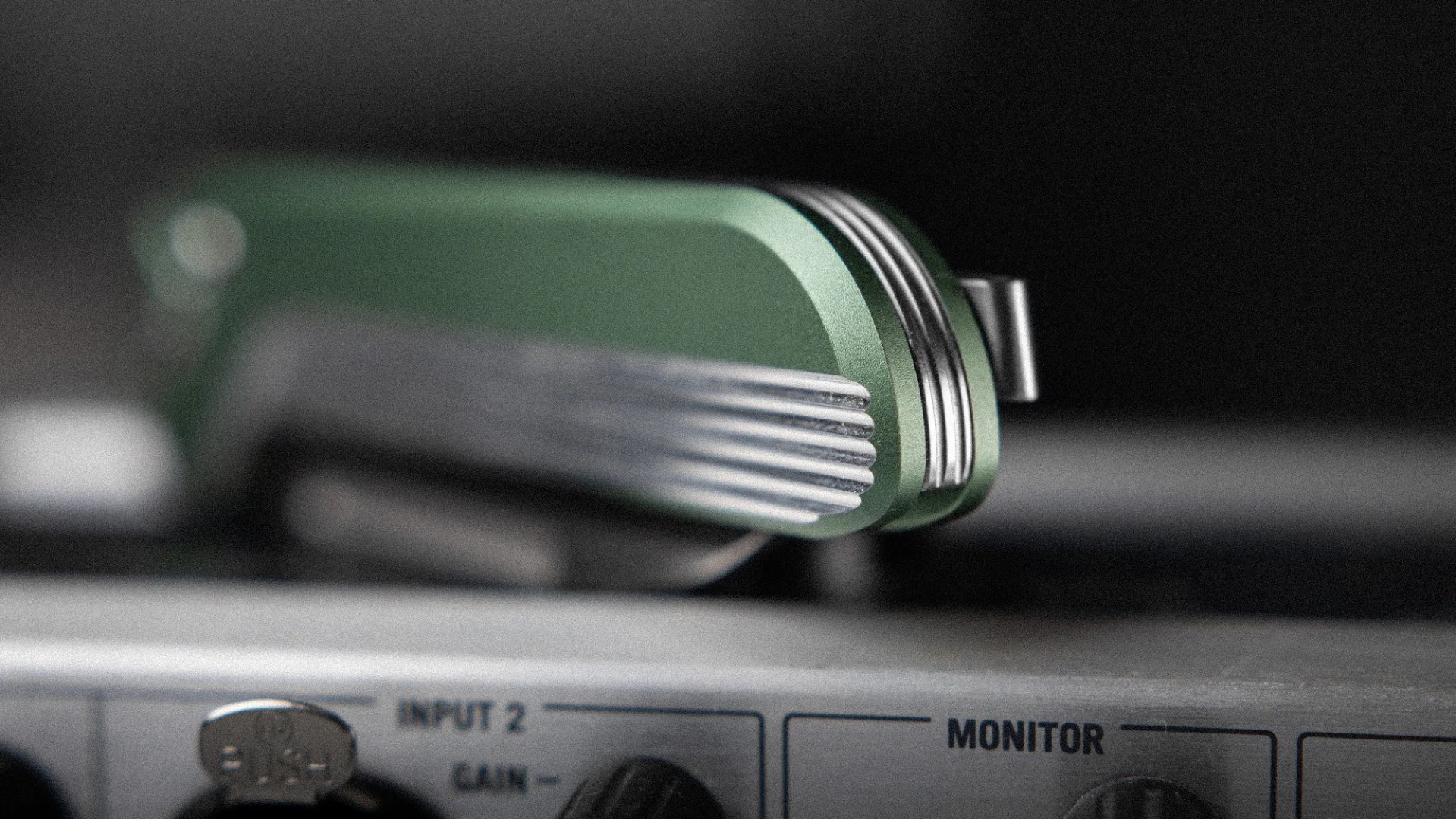 Close-up of a green and silver metal object resting on audio equipment labeled "INPUT 2" and "MONITOR.